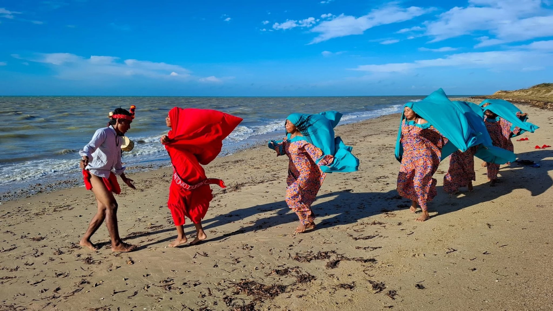 Mujeres wayuu danzan con mantas tradicionales rojas y turquesas a la orilla del mar en la Guajira venezolana