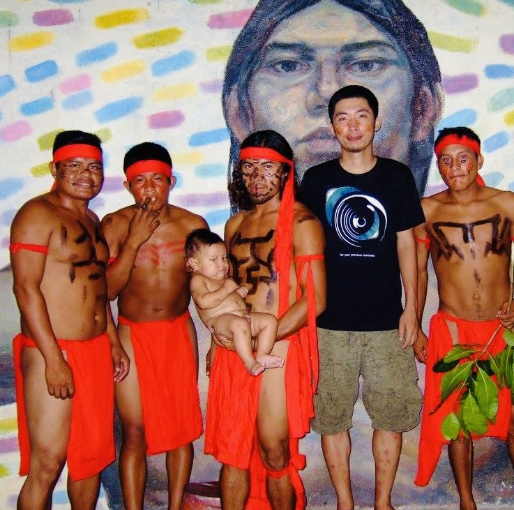 Grupo de jóvenes indígenas con pintura corporal tradicional frente al retrato pintado de un líder comunitario